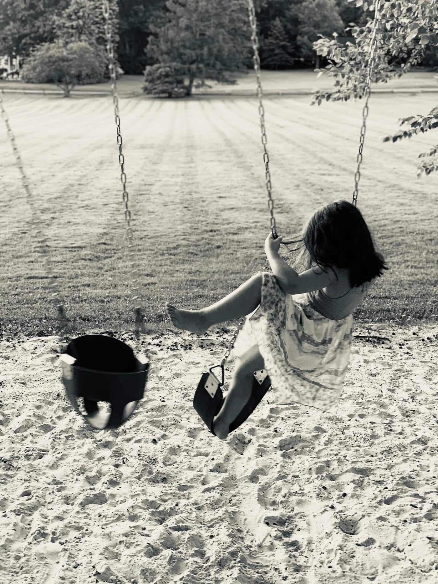 Black and white photo of a girl playing on a swing